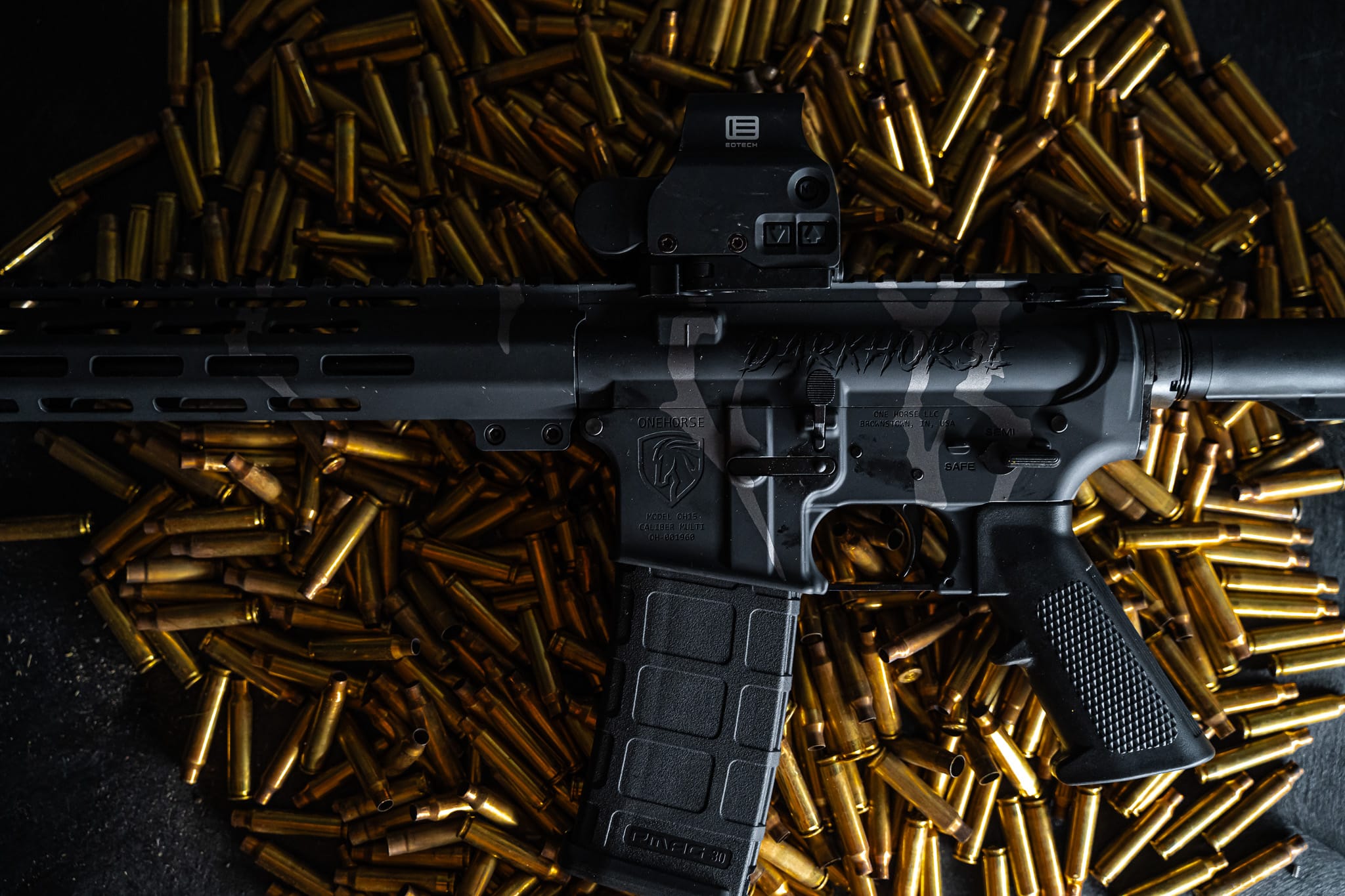 One Horse Model OH15 rifle with a camo finish and optic, resting on a bed of brass casings