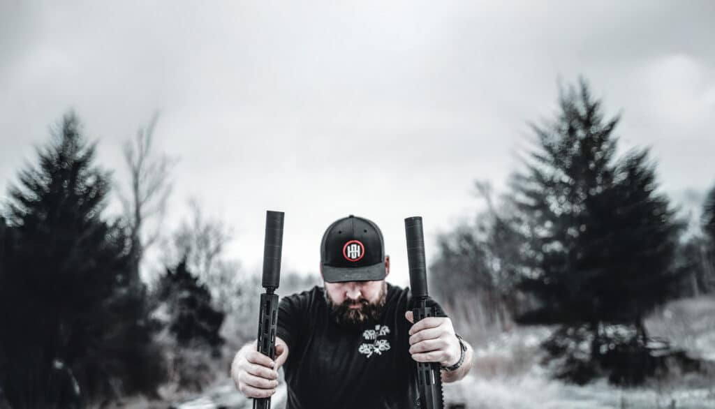 A man holding two American-made rifles outdoors, showcasing their craftsmanship and reliability in a natural setting.