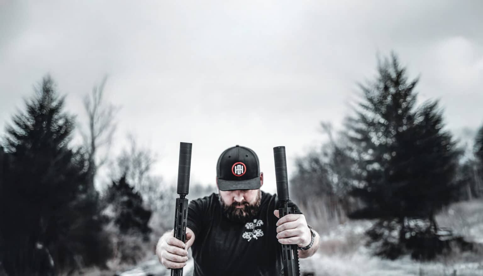 Man holding two rifles fitted with One Horse titanium Ashe and Ryn suppressors outdoors in winter