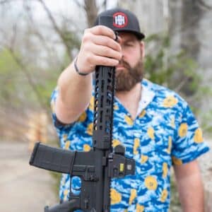 A man holds a black American-made rifle featuring a modular handguard, EOTech optic, and suppressor, showcasing reliable, high-quality craftsmanship.