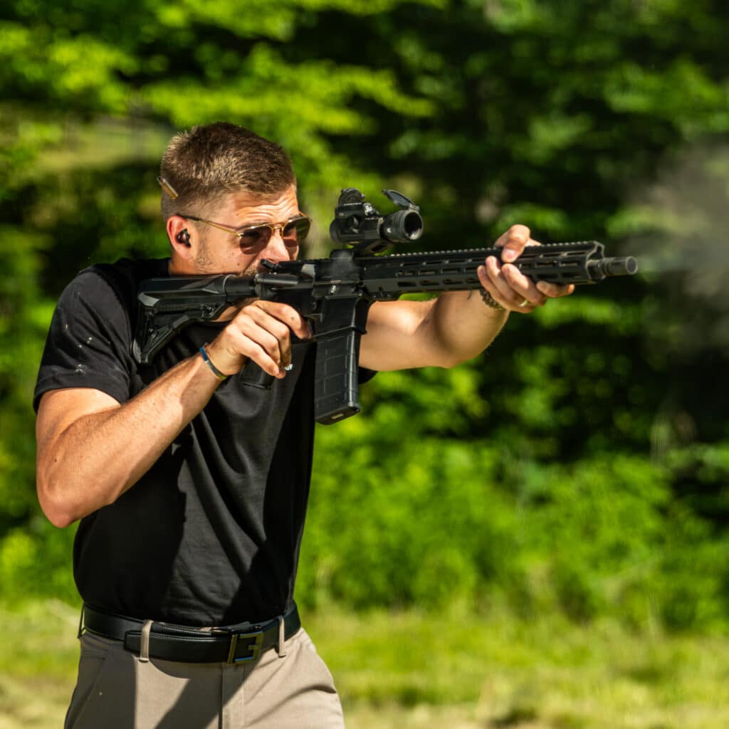 A shooter aiming an American-made rifle with a tactical scope, showcasing precision and reliability in a natural outdoor setting.