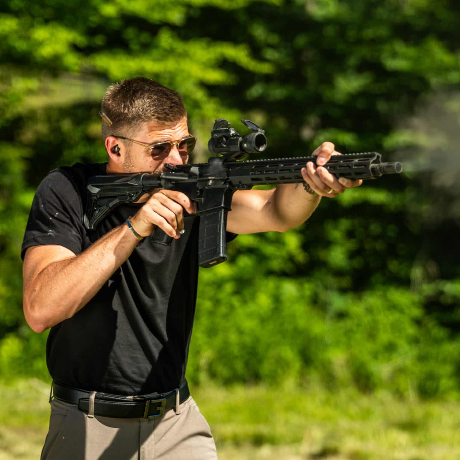 Shooter in sunglasses aiming a black One Horse AR-15 rifle with a red dot sight outdoors
