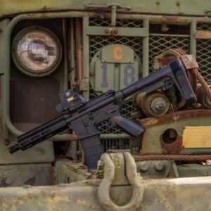A black American-made AR-style pistol with an EOTech optic, resting on a rugged, weathered military vehicle, showcasing durable, reliable construction.