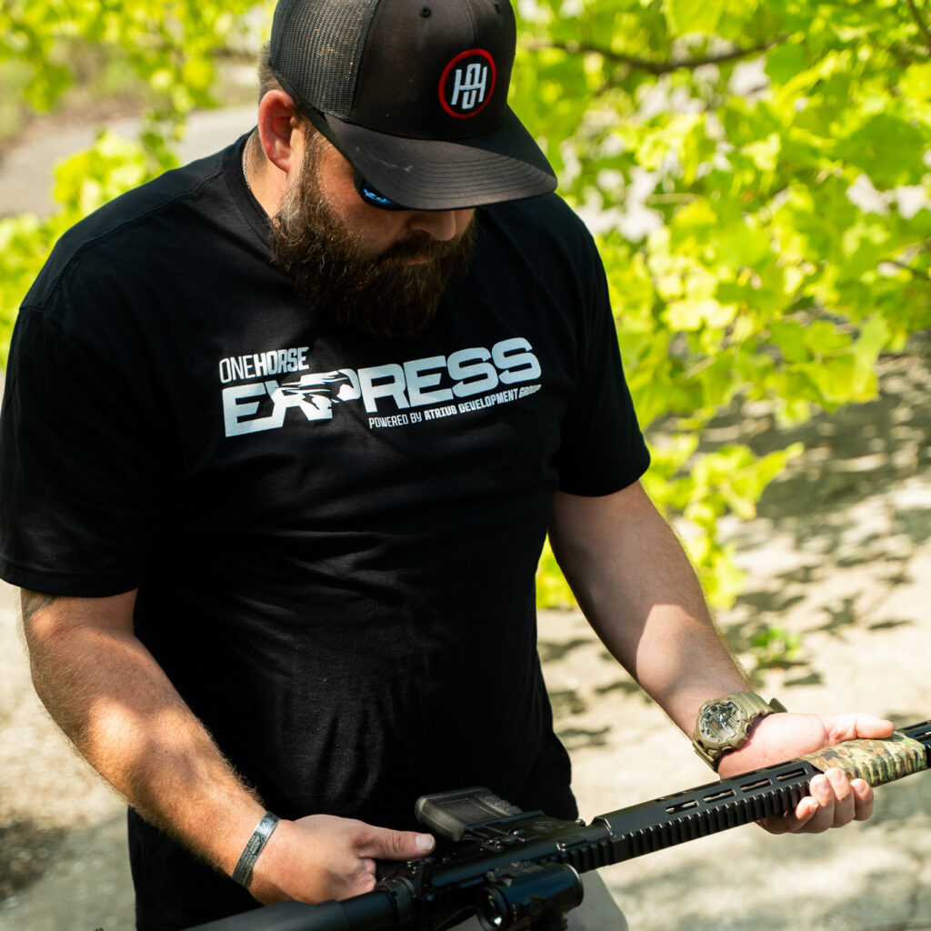 Man in a One Horse Express t-shirt and One Horse cap checking over a One Horse Express rifle