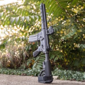 A reliable One Horse American-made rifle featuring a black finish, modular handguard, and Vortex optic, standing upright against a lush green backdrop.