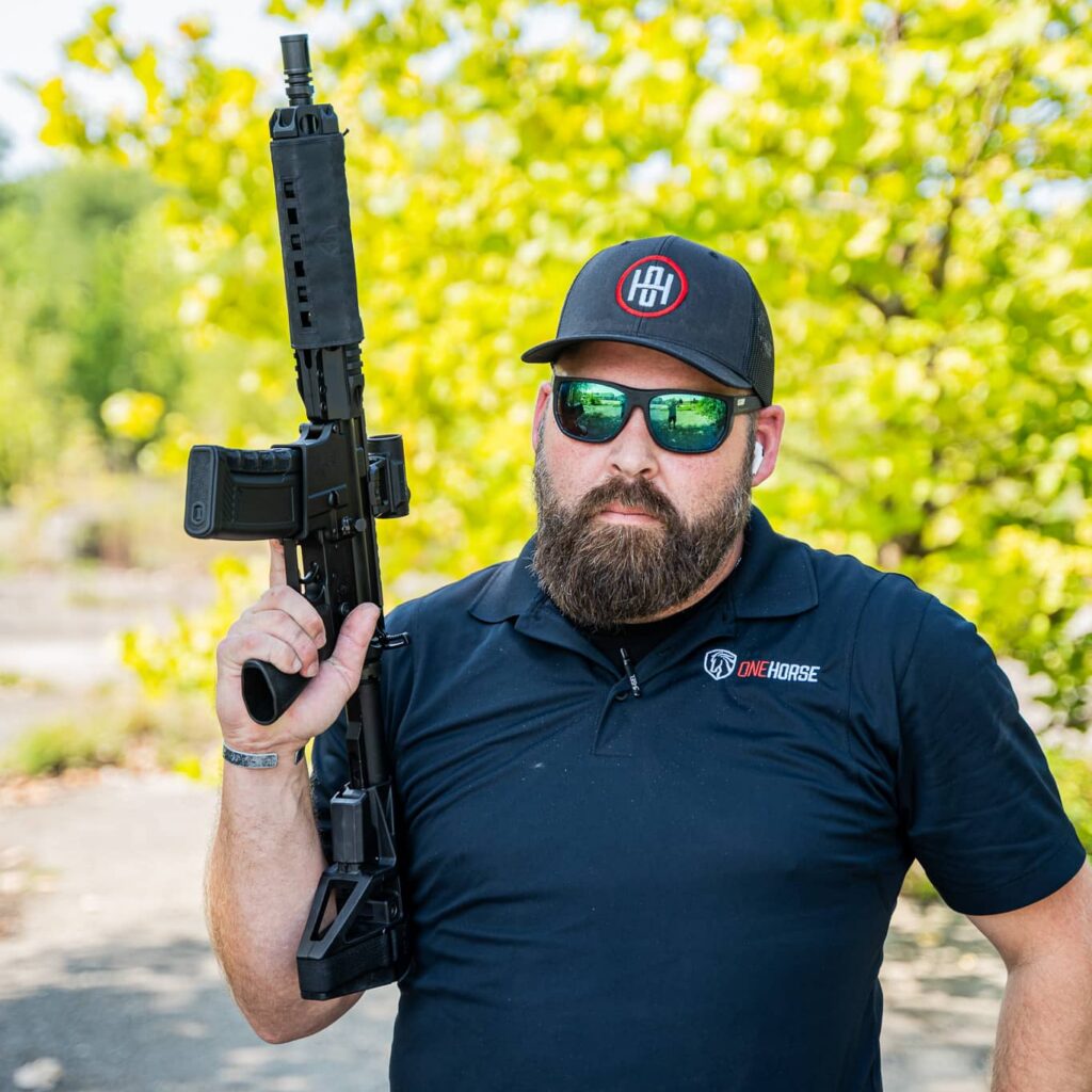 Man in a One Horse polo shirt and One Horse cap holding a black One Horse AR-15 outdoors